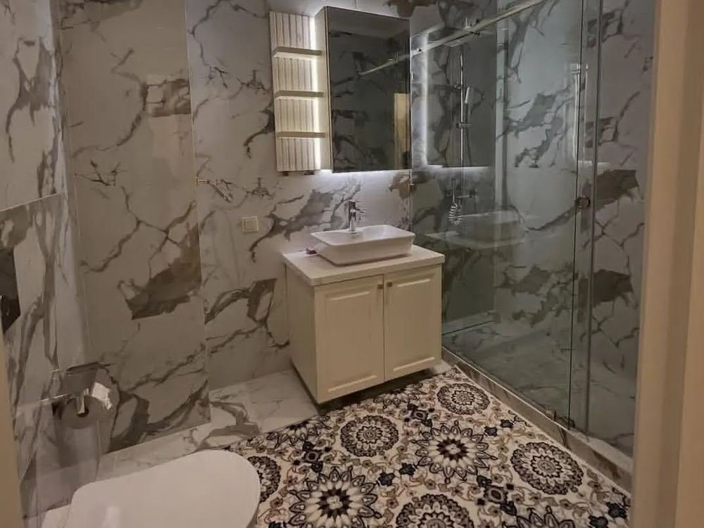 A bathroom with marble wall tiles and a patterned tiled floor
