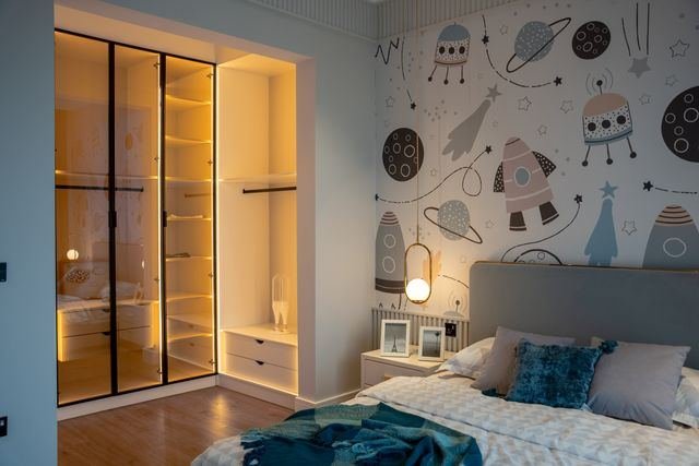 A child's bedroom with a lit fitted wardrobe and a mural wall