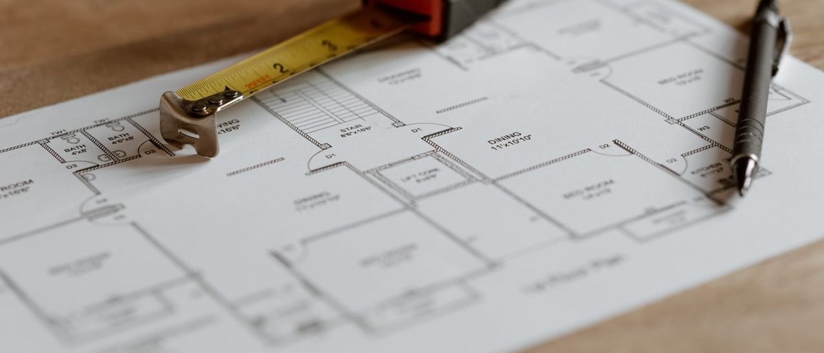 A floor plan on a desk with a tape measure and a pen