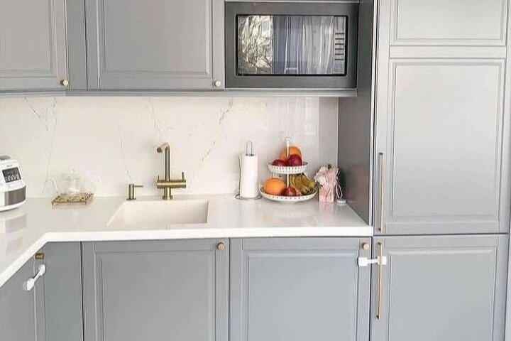 A grey shaker kitchen with a brass tap and white worktop