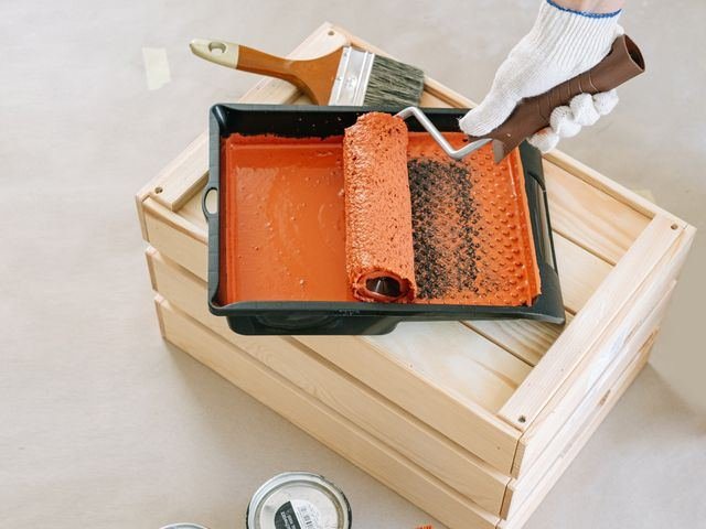A paint roller and tray with orange paint on a dust sheet