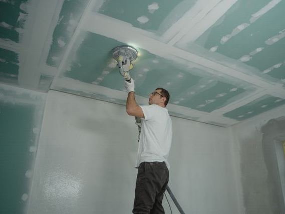 A worker sanding a newly boarded ceiling