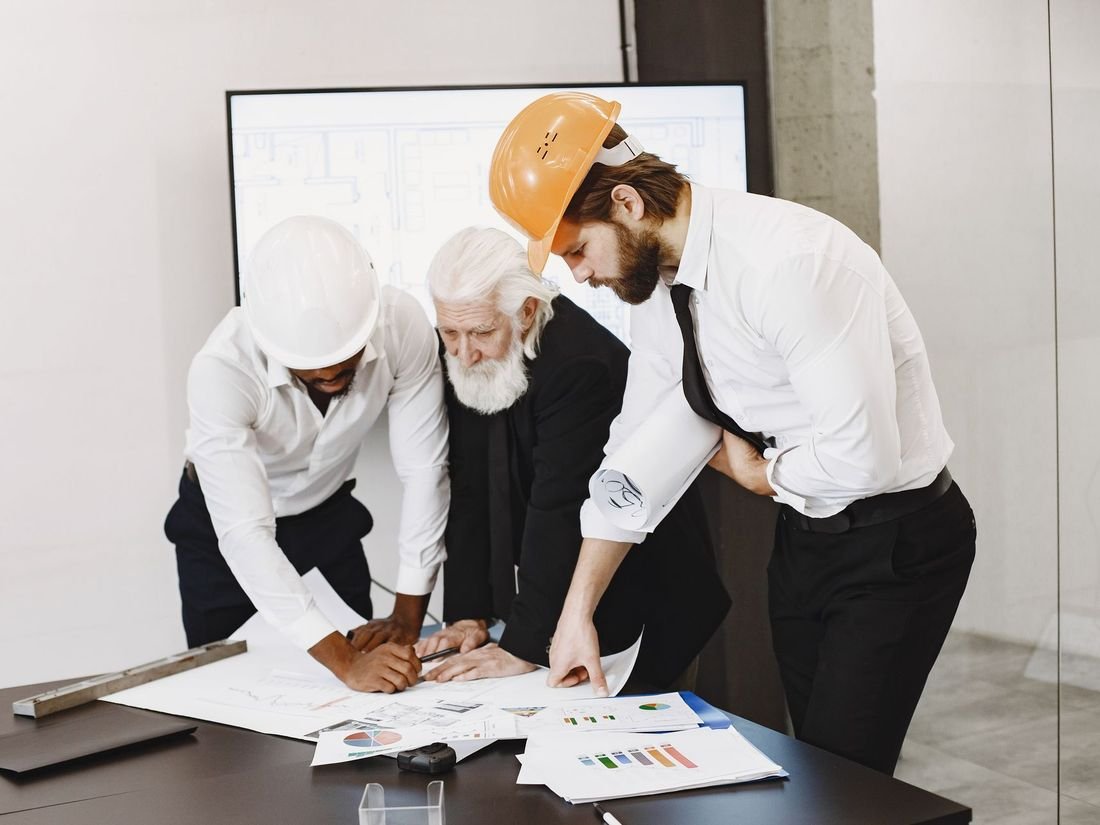 Three people in hard hats studying building plans together